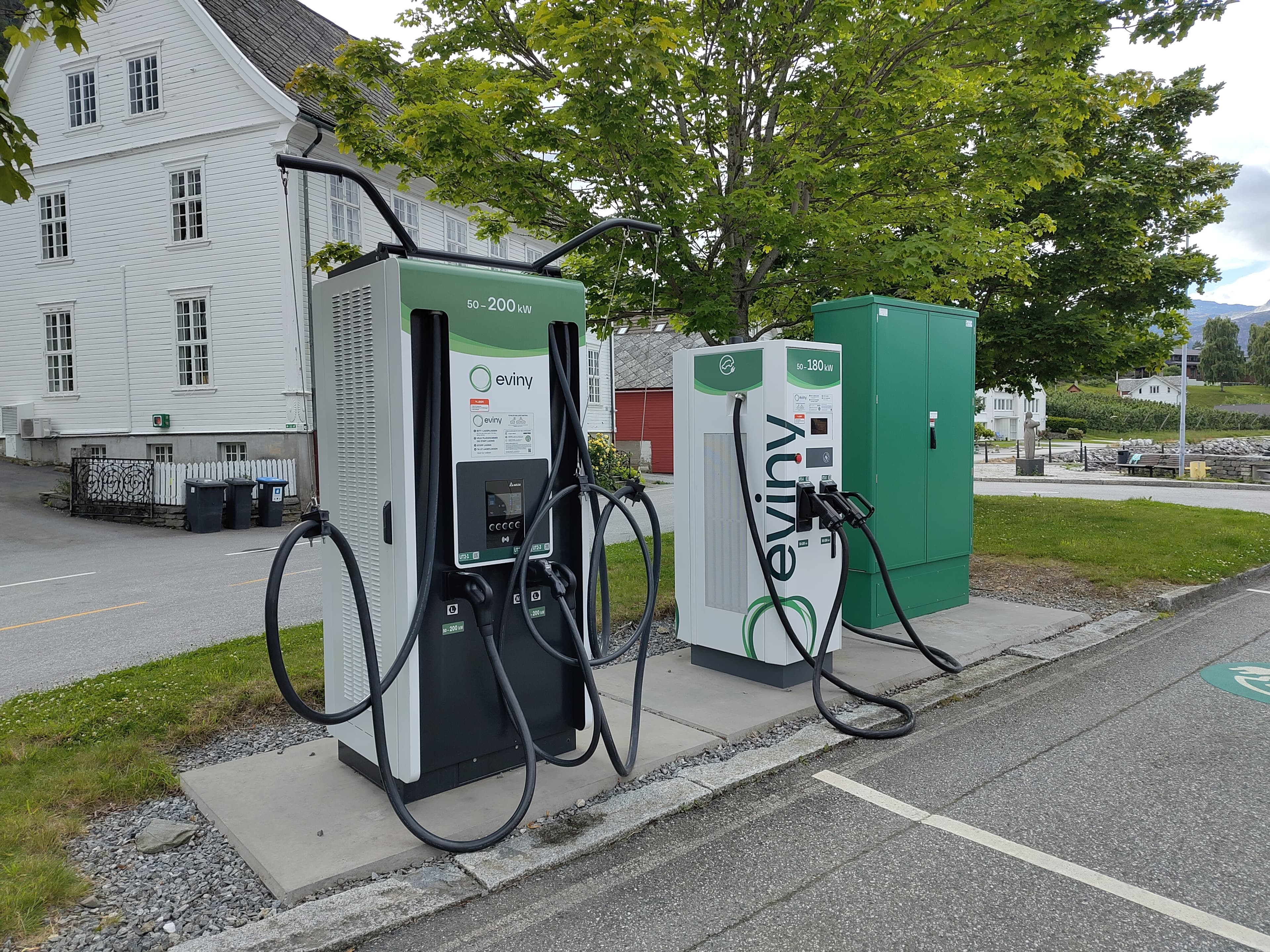 An electric vehicle charging station beside a road in Utne, Norway, with hills in the background.