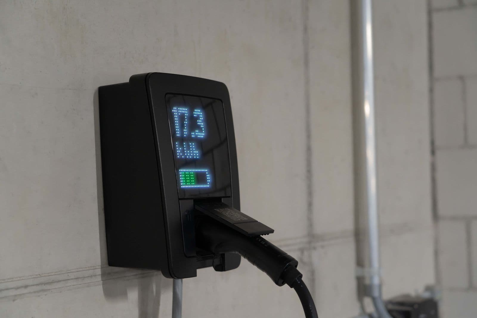 A black wall-mounted electric car charger in a garage, its screen showing 17.3 kWh delivered.