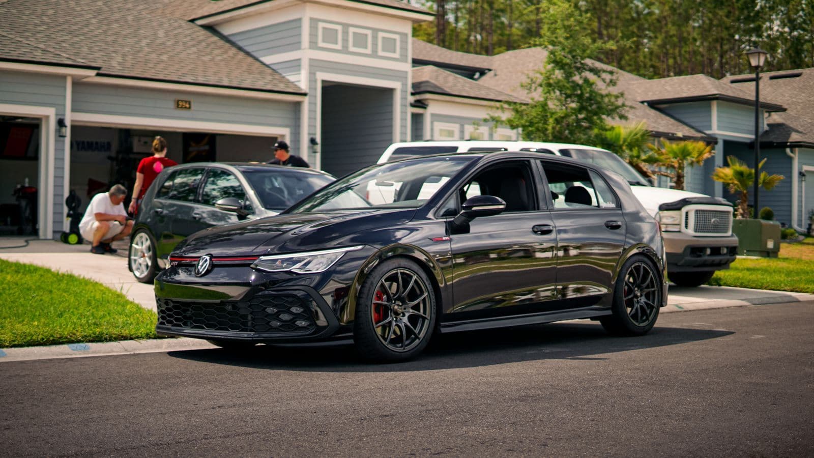 A black hot hatch parked in front of a house while two more cars are being washed in the driveway behind it.