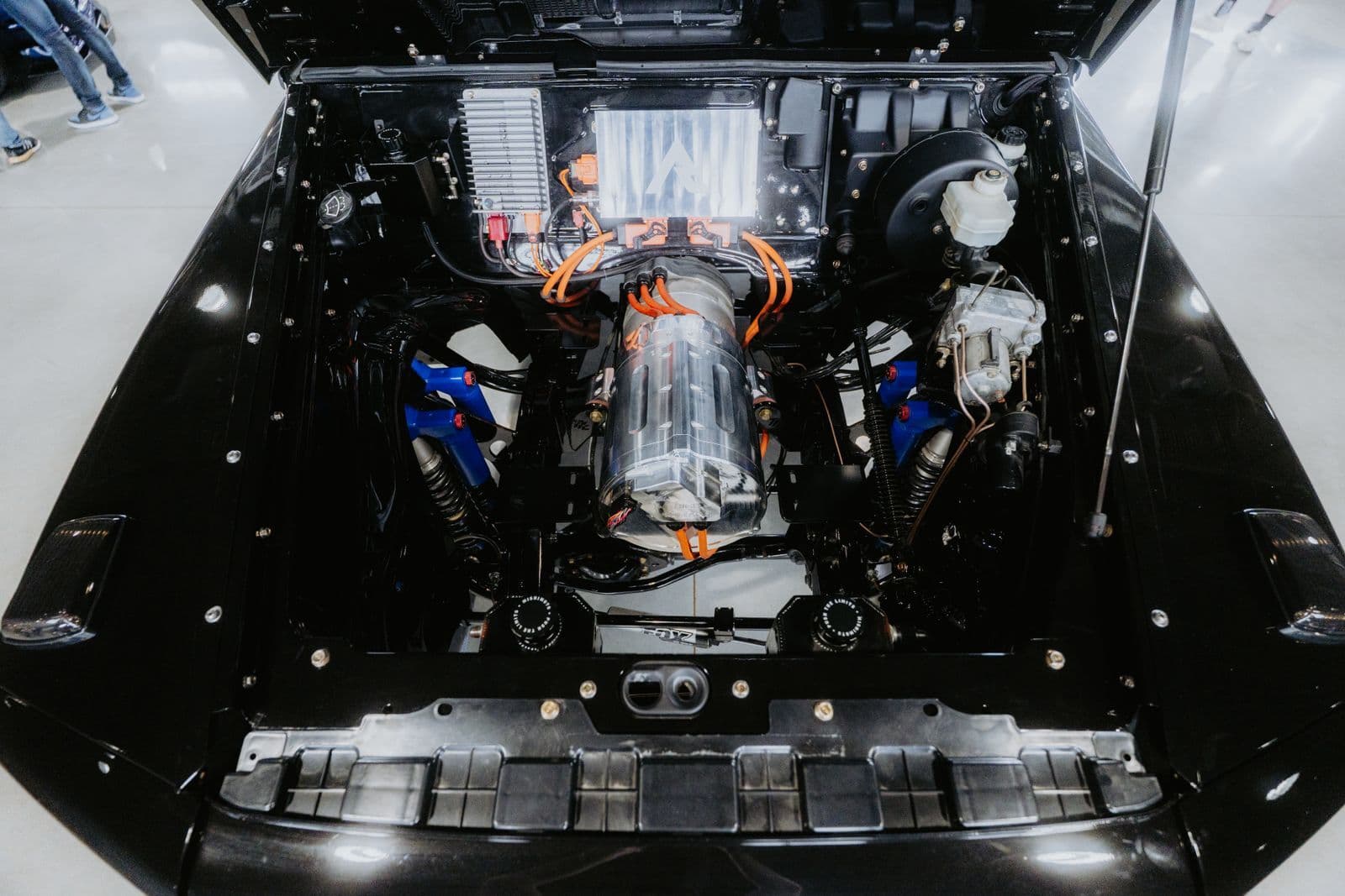 An open bonnet revealing an electric drive unit wrapped in bright orange high-voltage cables alongside blue and silver components.