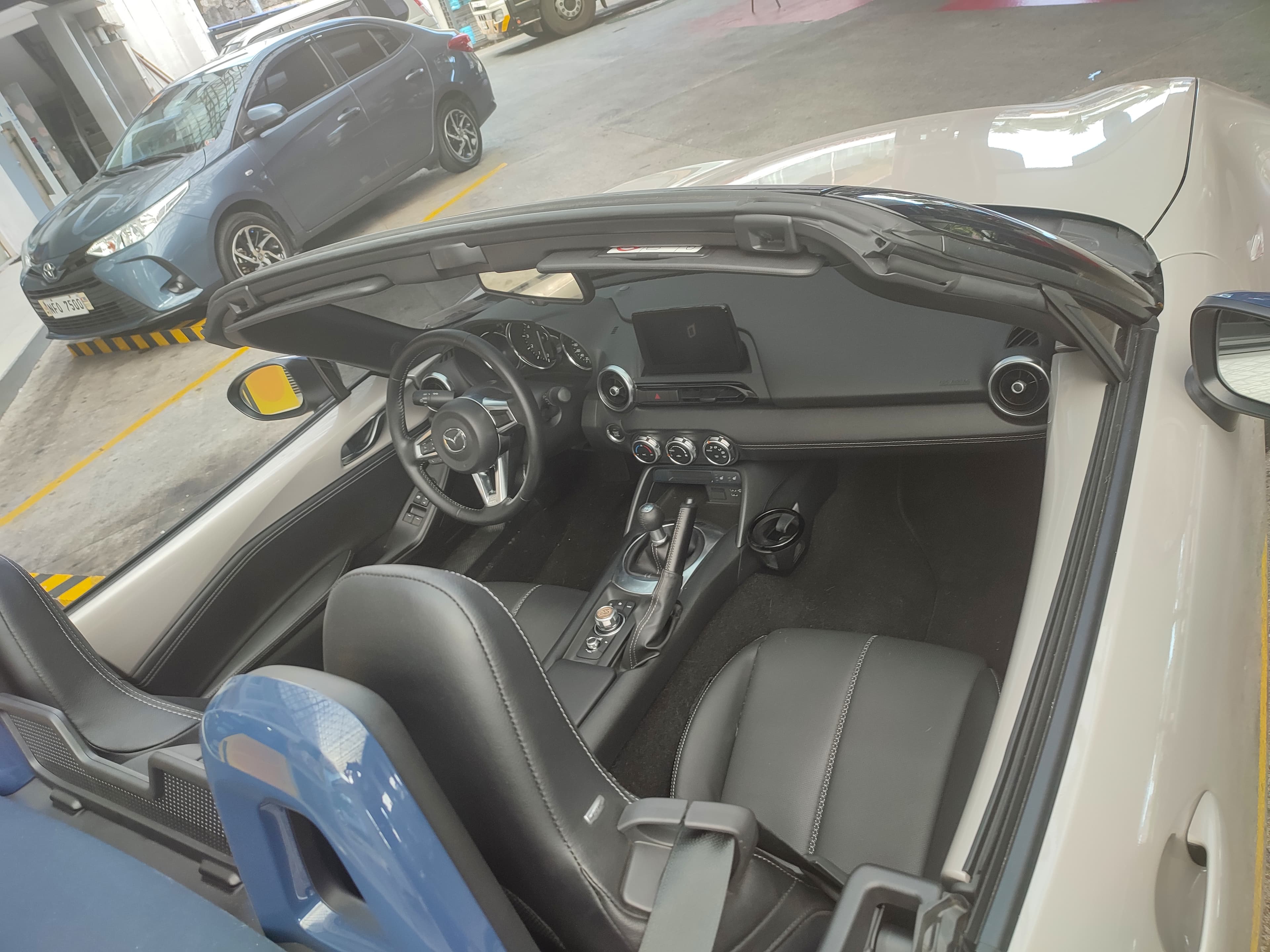 The dashboard of a Mazda MX-5, with a small central screen above three round physical climate-control knobs.