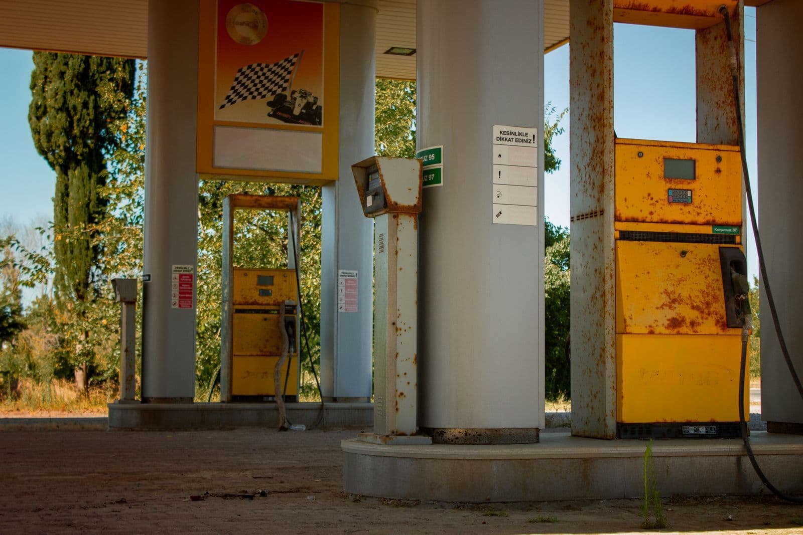 Two rusting yellow fuel pumps standing under the concrete canopy of a long-closed service station.