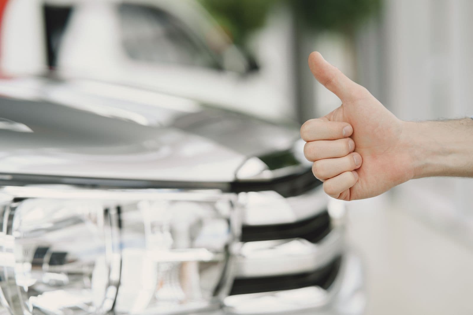 A hand giving a thumbs-up beside the headlight and bonnet of a silver car.