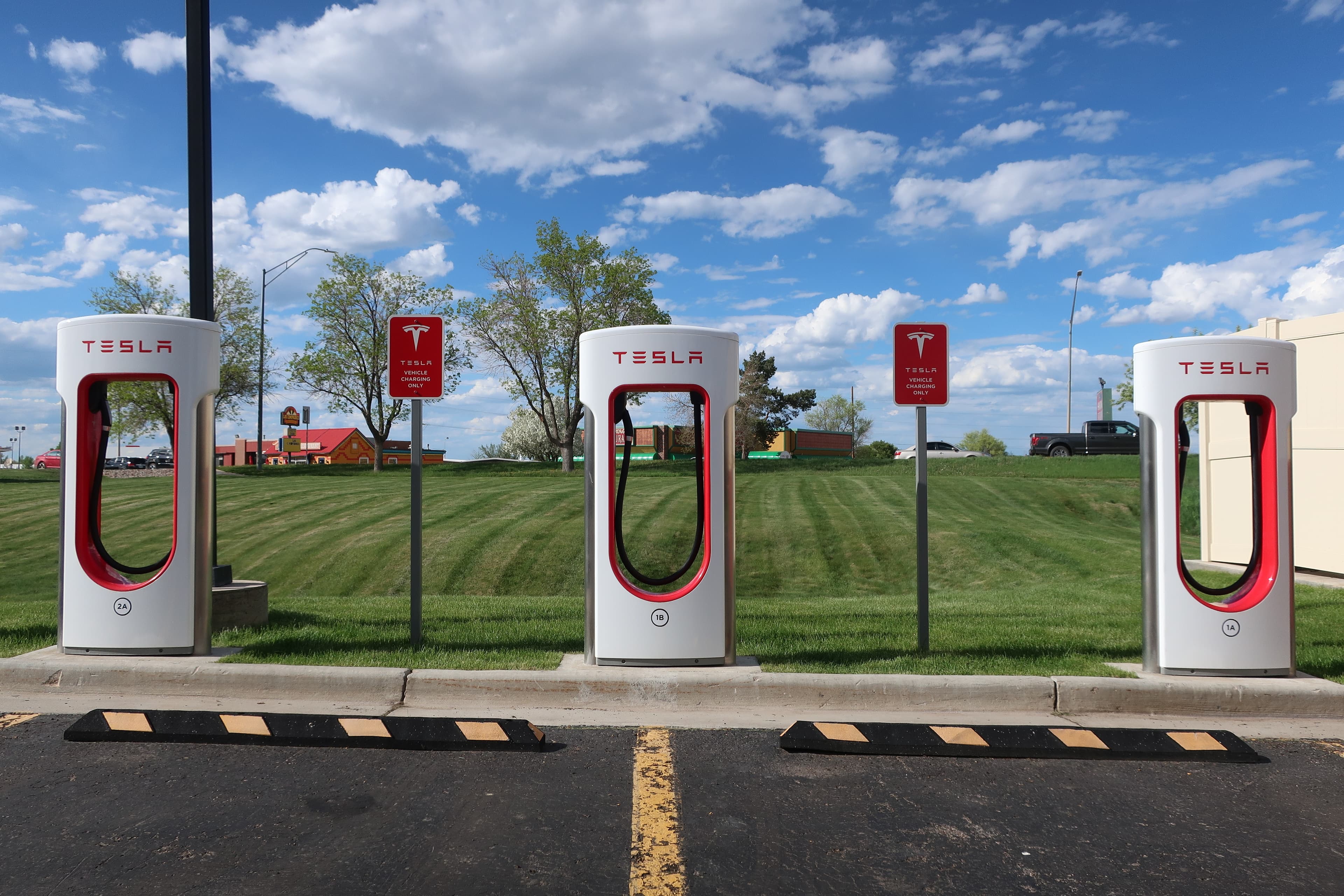 A Tesla Supercharger station with red and white charging stalls under a wide sky in Gillette, Wyoming.