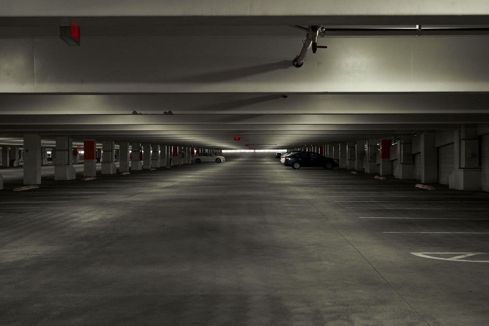 A dimly lit, almost empty level of a multi-storey car park with a couple of cars left in the bays.