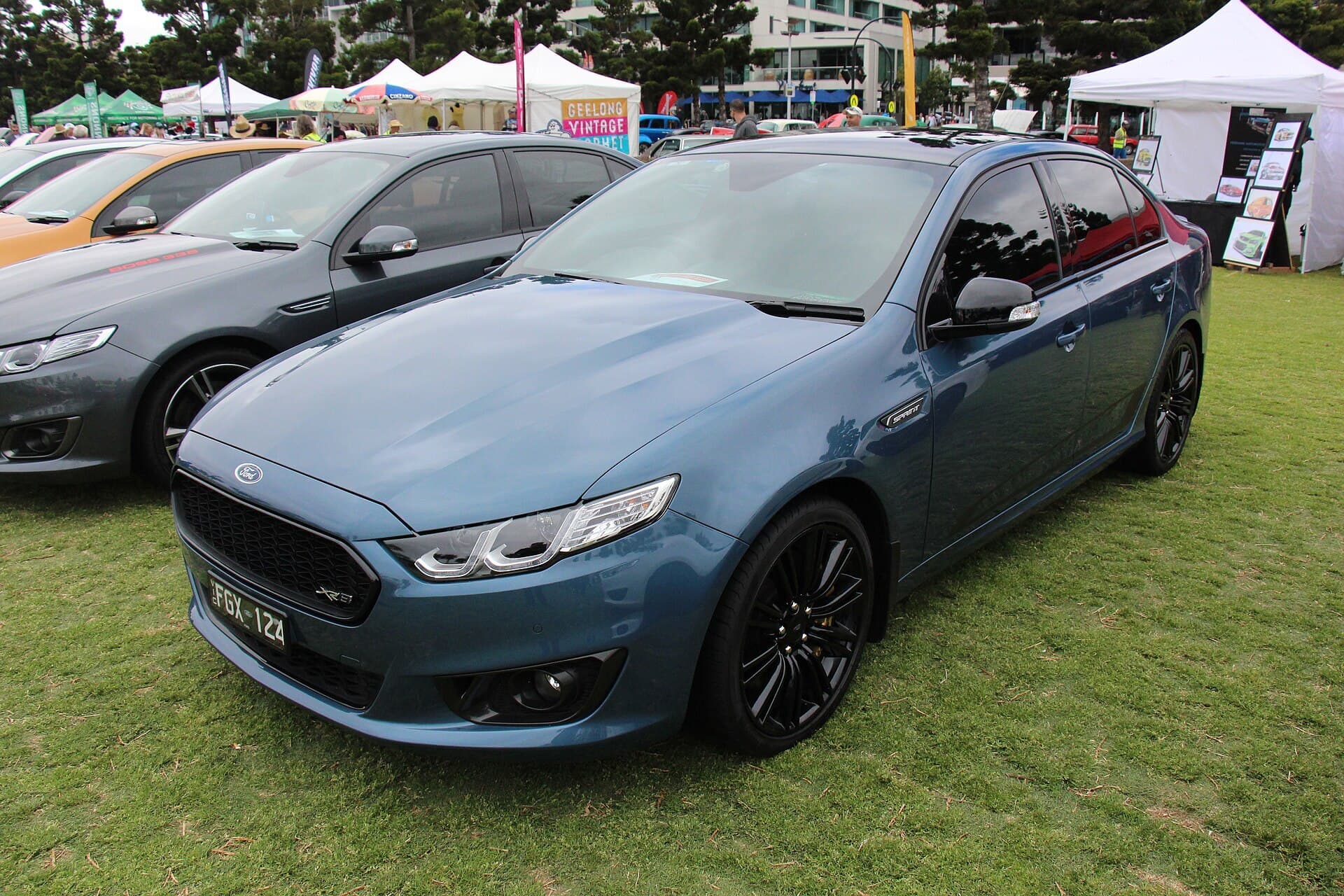 A light blue Ford FG X Falcon XR8 Sprint sedan with dark wheels and bonnet stripes, parked outdoors.
