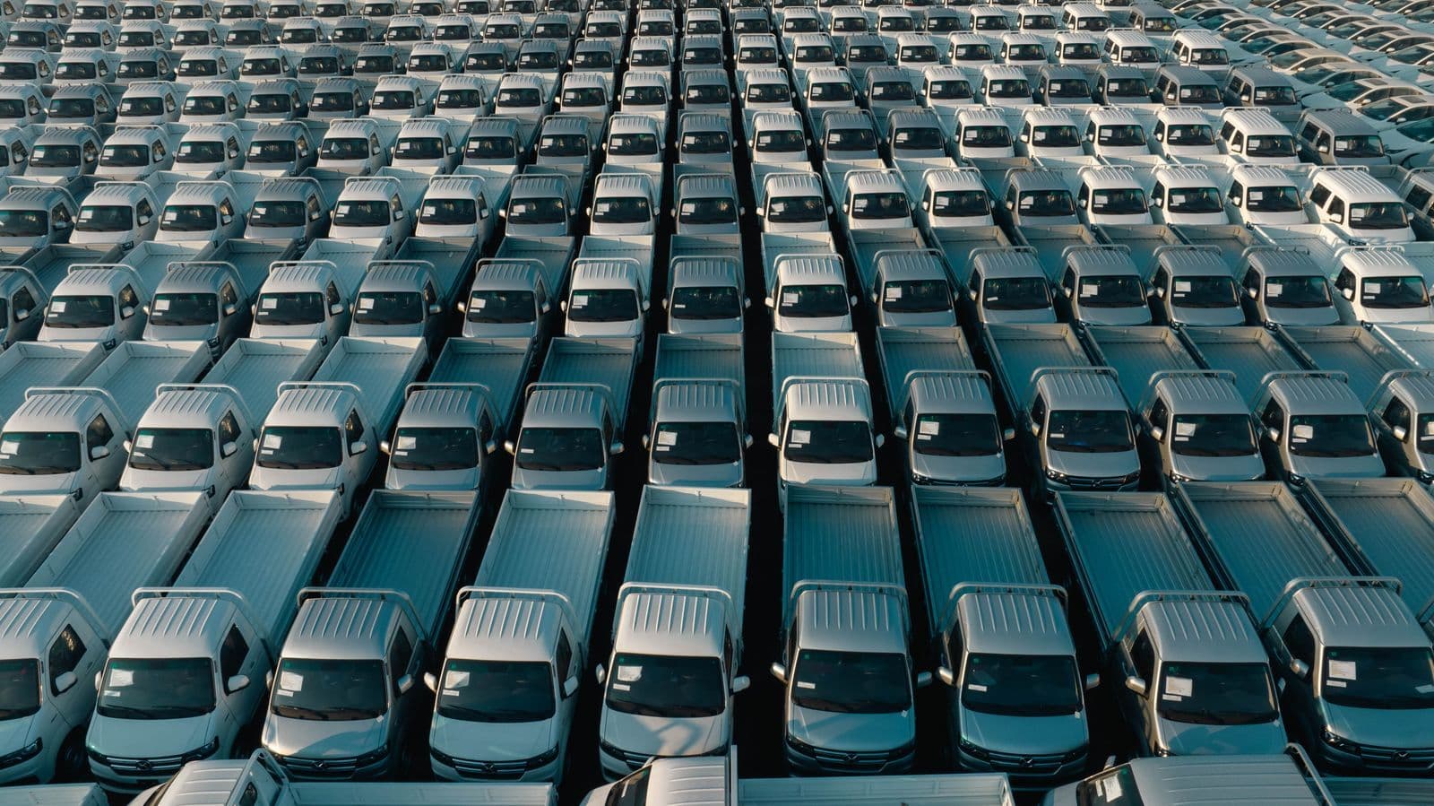 An aerial view of hundreds of identical white utes parked in tight rows across a storage yard.