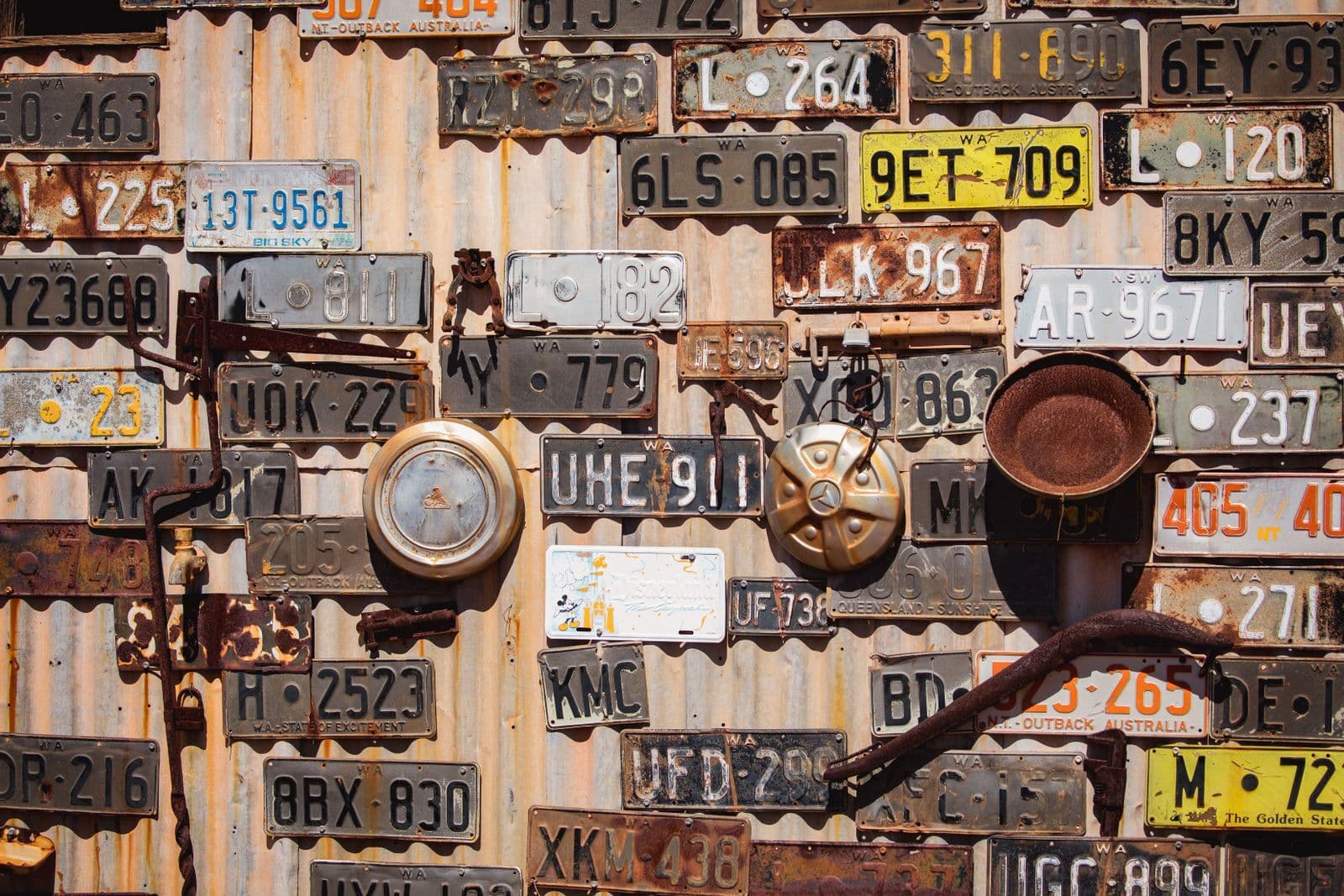 Dozens of old Australian number plates nailed in rows across a rusting corrugated iron shed wall.