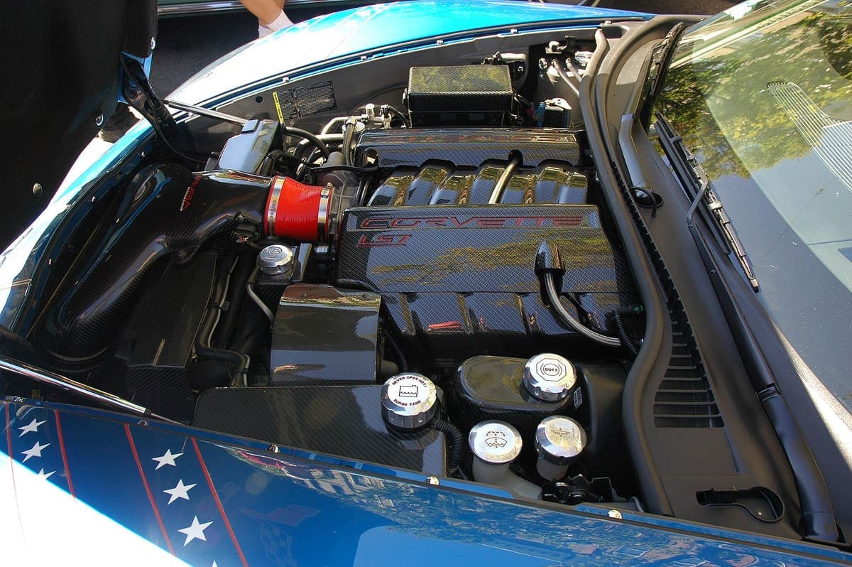 A modern engine bay seen from above, with the engine largely hidden beneath carbon fibre covers, moulded plastic ducting and braided hoses rather than exposed metal