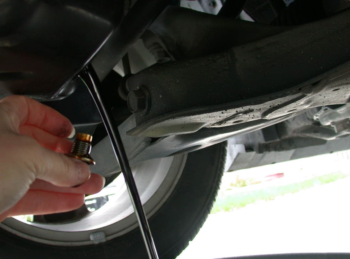 Dark used engine oil draining from a sump plug into a collection pan beneath a car