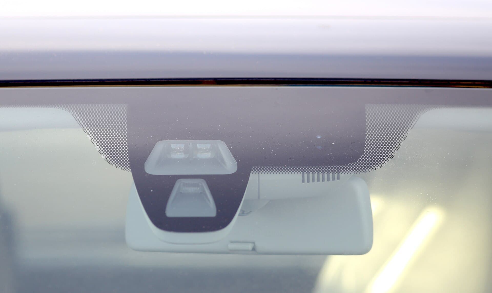 A sensor module mounted behind the glass at the top of a car windscreen, above the rear-view mirror.