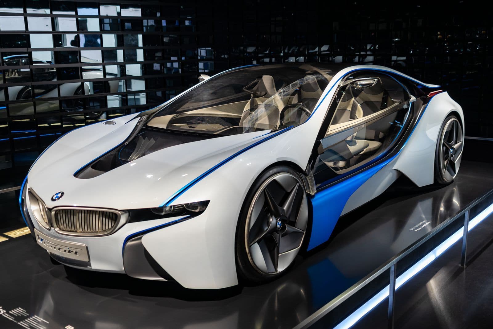 A white and blue BMW i8 hybrid sports car on a polished showroom floor under spotlights.