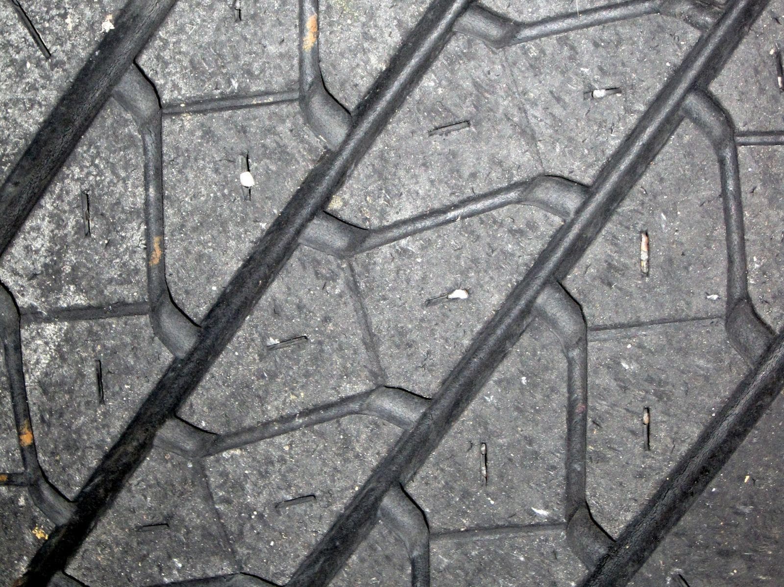 A close-up of a worn car tyre's tread blocks and grooves with small stones lodged in them.