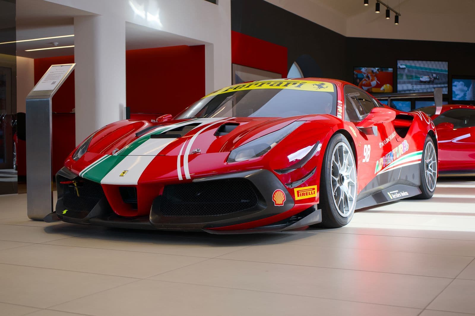 A red Ferrari race car with green, white and red stripes and sponsor decals on display in a showroom.