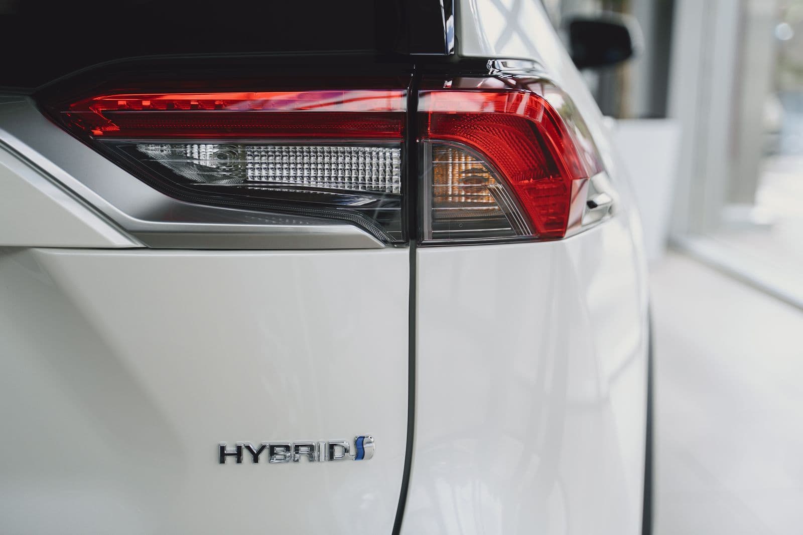 A chrome hybrid badge below the red tail light on the tailgate of a white SUV.
