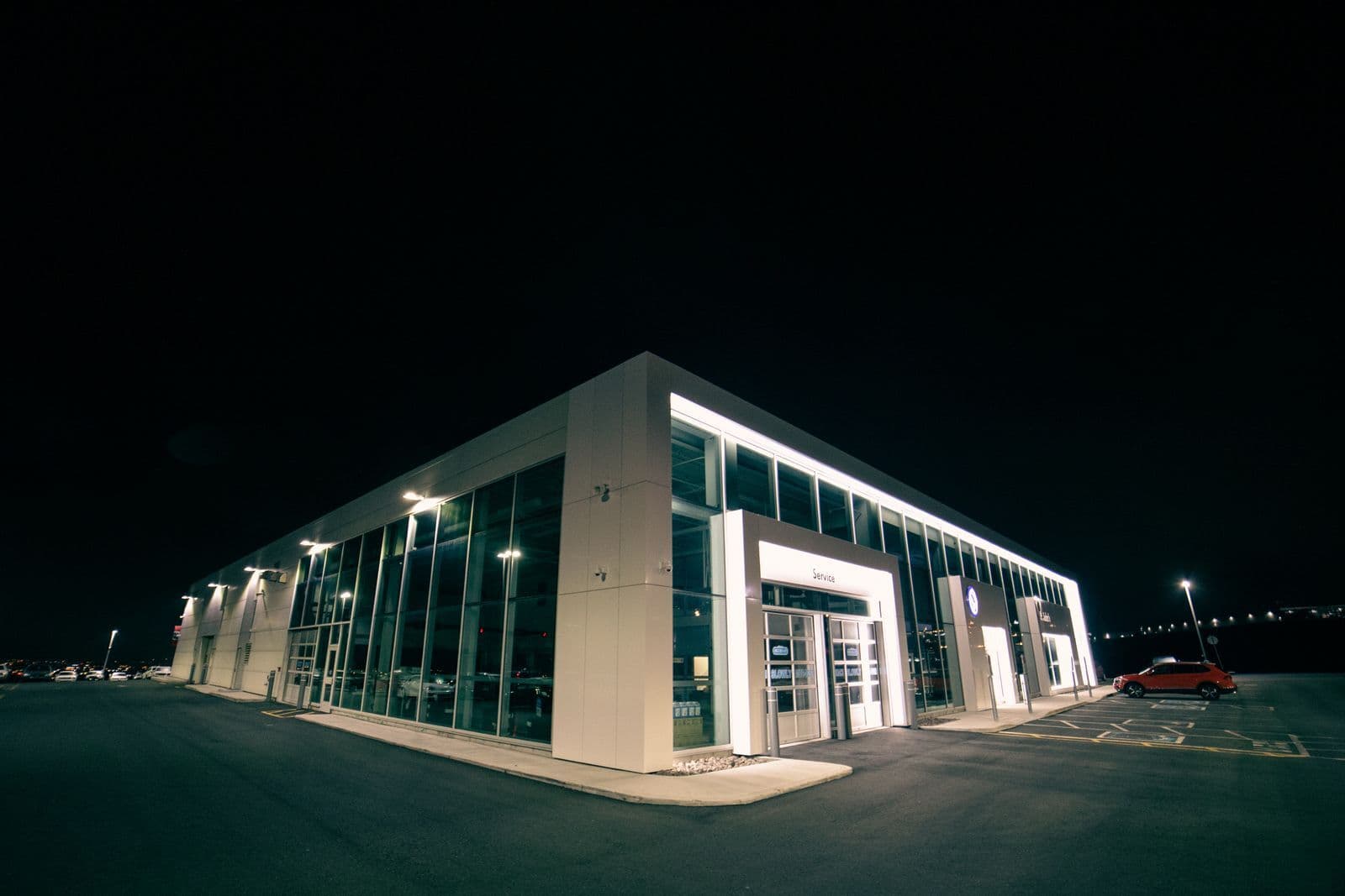 A brightly lit glass-fronted car showroom photographed from the corner of its forecourt at night.