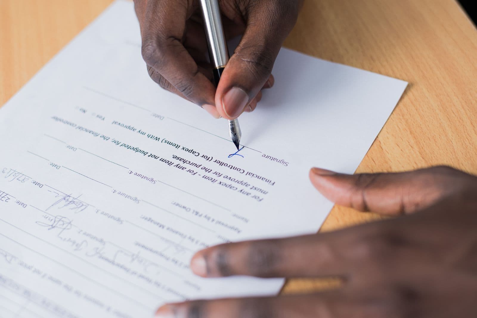 A hand signing a printed form with a fountain pen on a wooden desk.