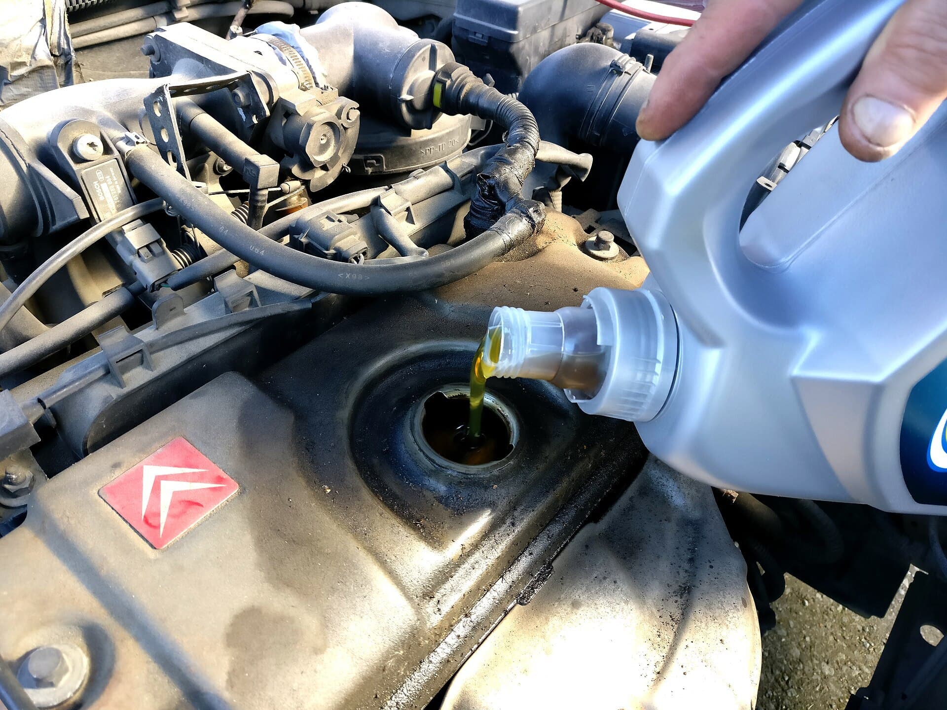 Golden engine oil being poured from a plastic bottle into the oil filler of a car engine