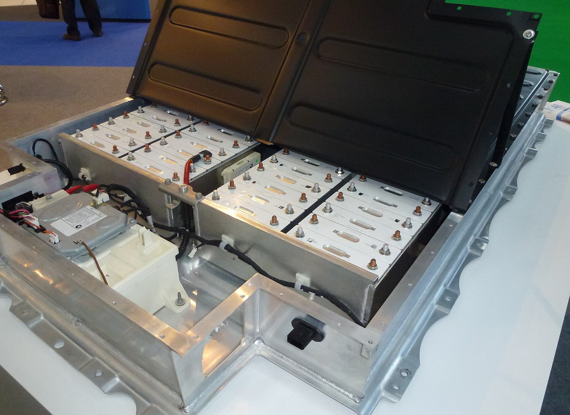 An open electric-car battery pack with rows of silver lithium-ion modules in an aluminium tray, its black lid propped up.