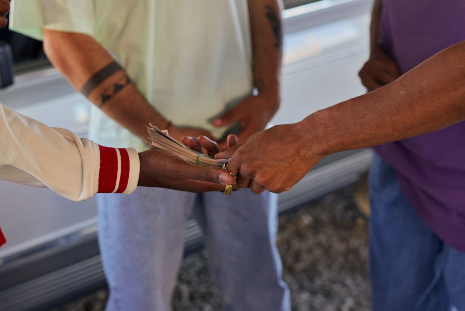 A close-up of a folded wad of banknotes being passed from one person's hand to another's outdoors.