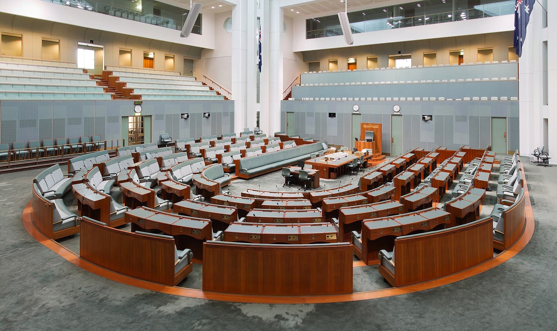 The empty House of Representatives chamber at Parliament House in Canberra, with curved rows of green seats and timber desks.