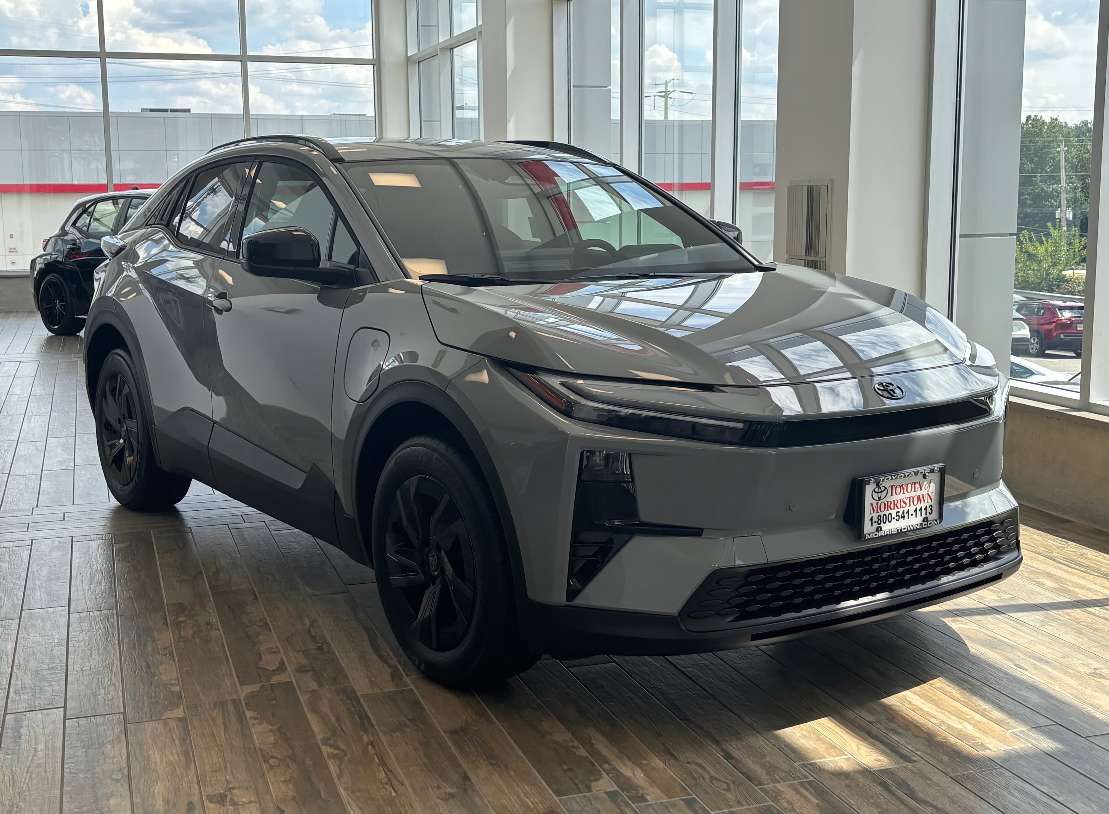 A grey 2026 Toyota C-HR electric SUV parked in a dealership showroom, photographed from the front right.