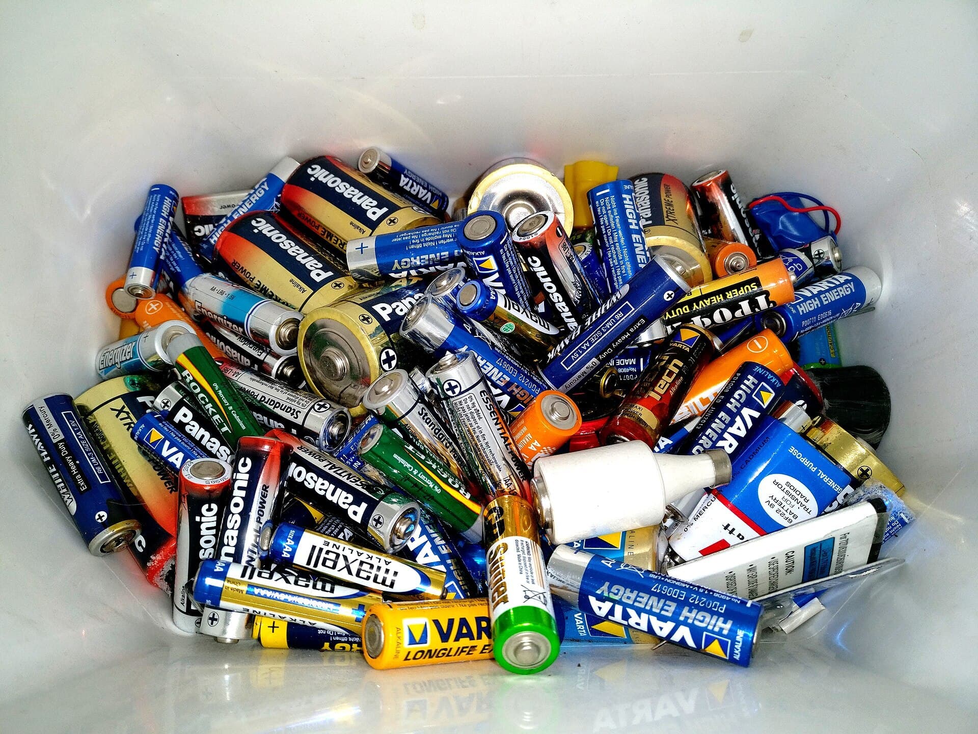 A white plastic bin filled with used AA, C and D batteries of various brands.
