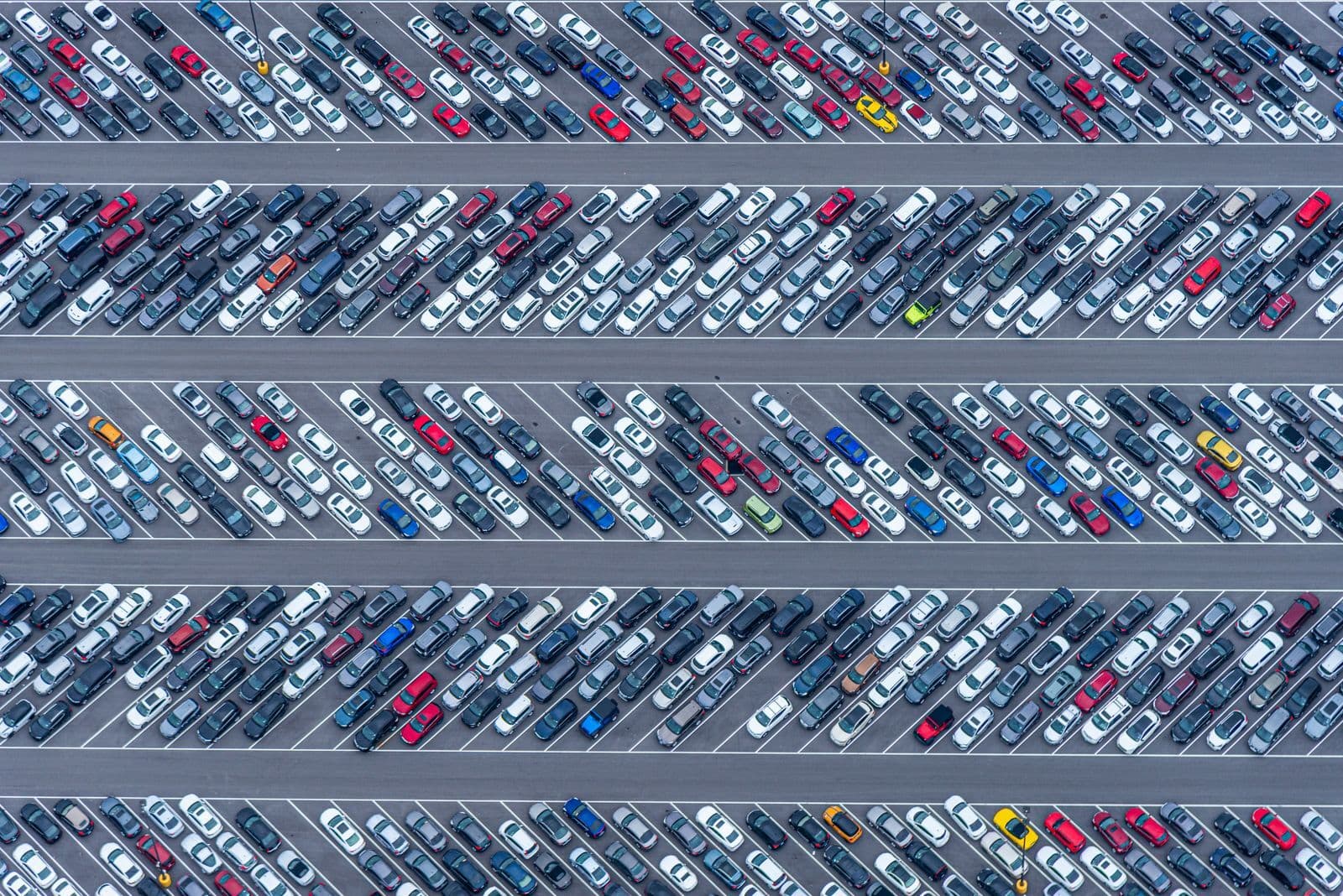 An overhead view of hundreds of cars packed in diagonal rows across a large sealed lot.