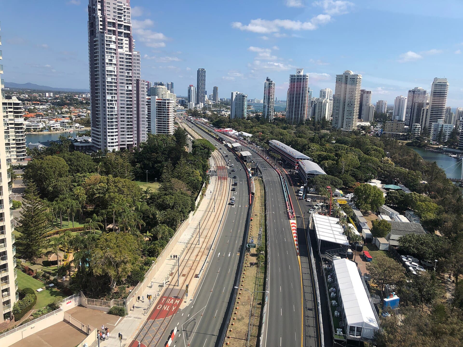 An aerial view of Surfers Paradise high-rises with a street circuit, pit buildings and marquees set up beside a tram line and public road.