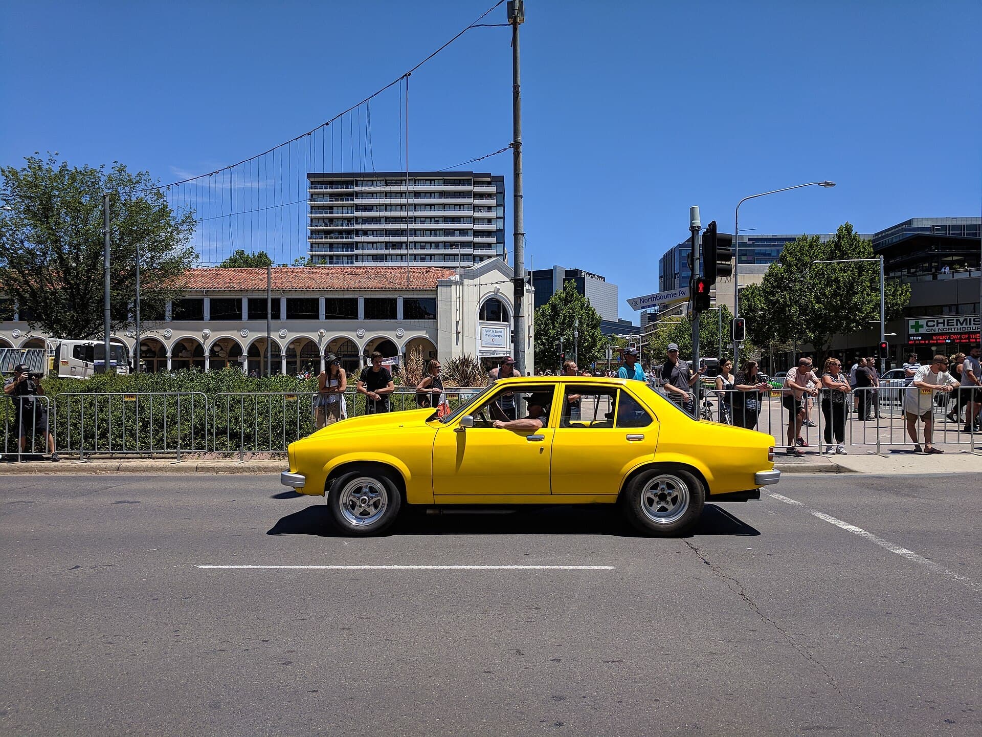 A bright yellow Holden Torana sedan driving in the Summernats street parade in Canberra, with spectators lining the road