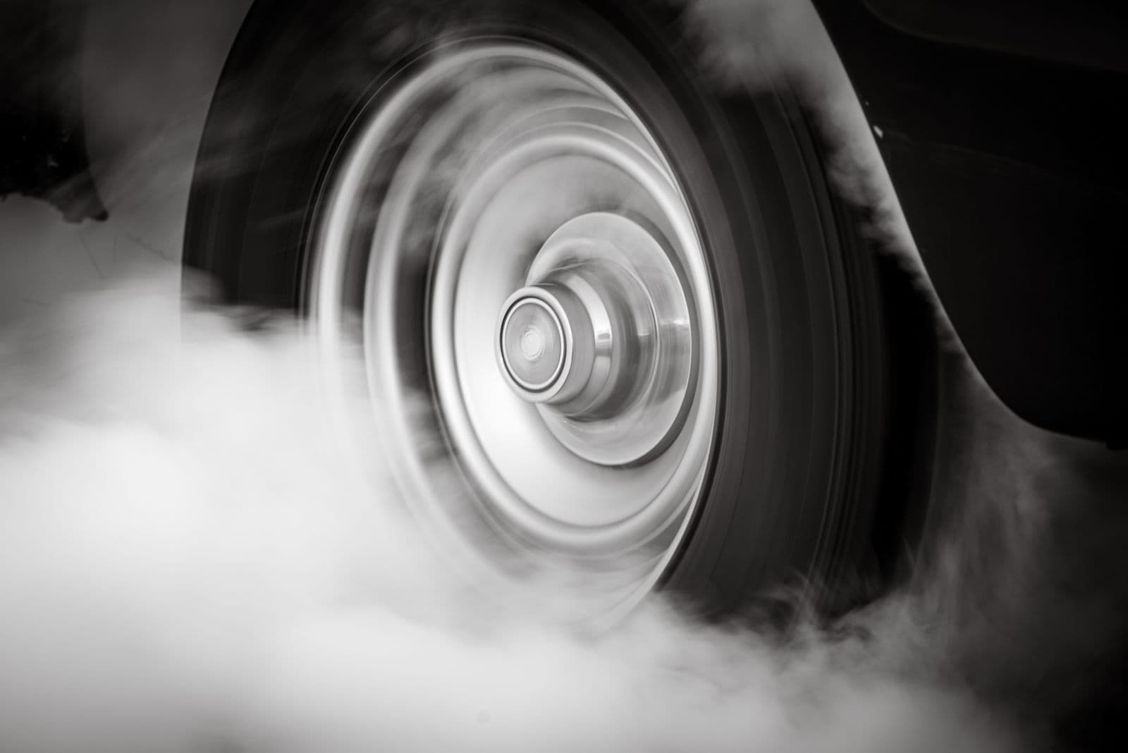A black-and-white close-up of a car wheel spinning in a cloud of tyre smoke.