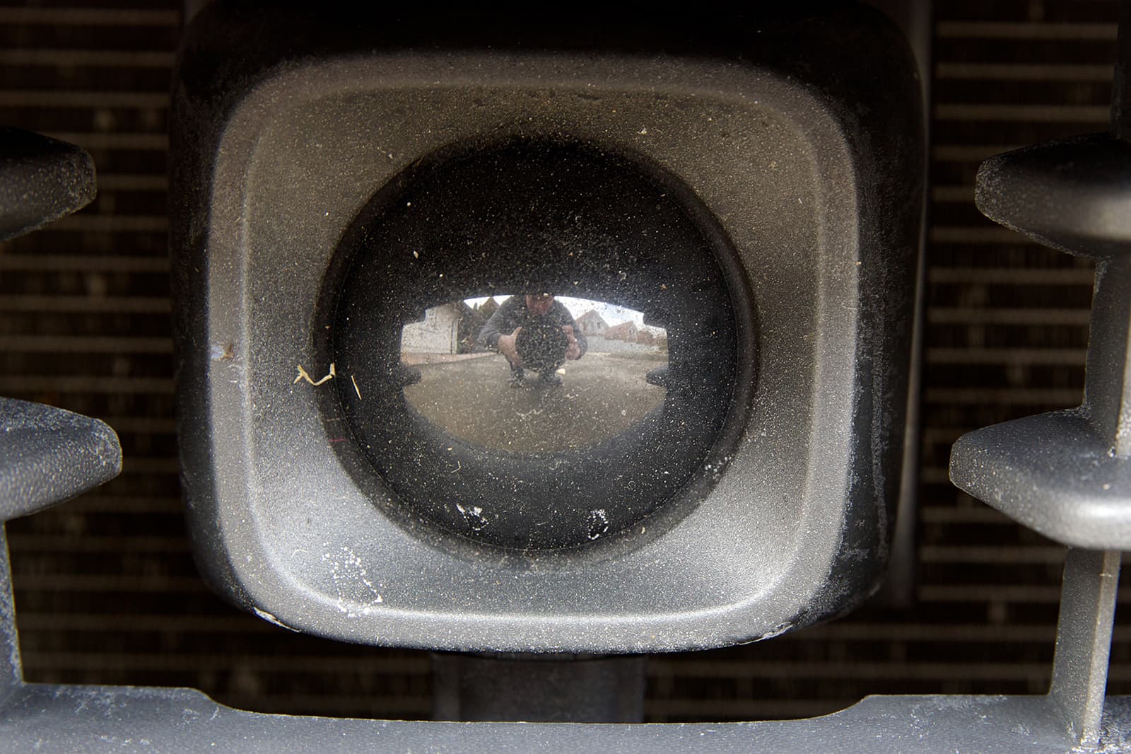 Close-up of a square, dust-covered sensor housing with a round face, set into a car's lower front grille.